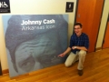 An unidentified male worker kneeling next to an exhibit board of Johnny Cash's face from the eyes up