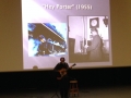 An unidentified male solo guitarist on stage with two images behind him: one of a train and one of a railroad porter