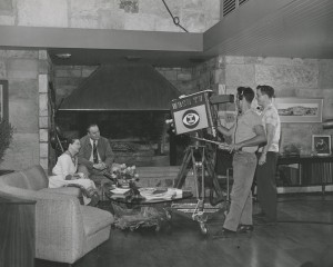 Winthrop and Jeannette sitting together near fireplace with WDSU-TV camera and crew filming them, Winrock Farms, 1957