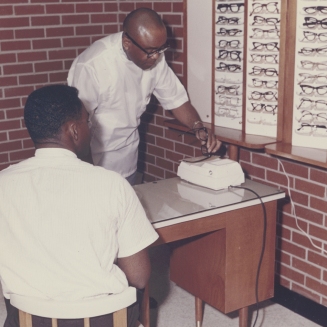 Dr. Townsend helps fit a patient with glasses at his clinic on Wright Ave, early 1980s