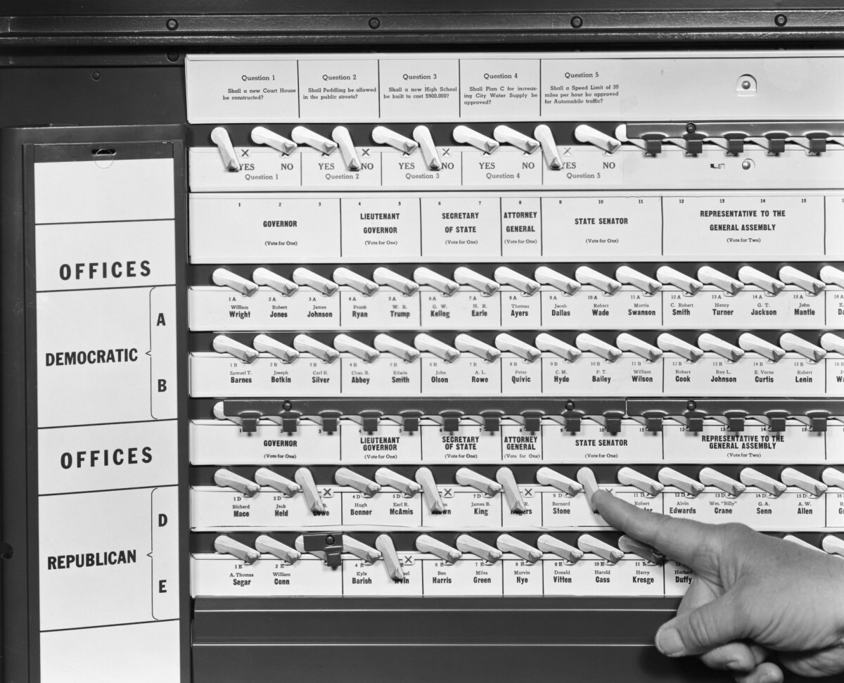 Photograph of a hand pushing a lever on a voting machine