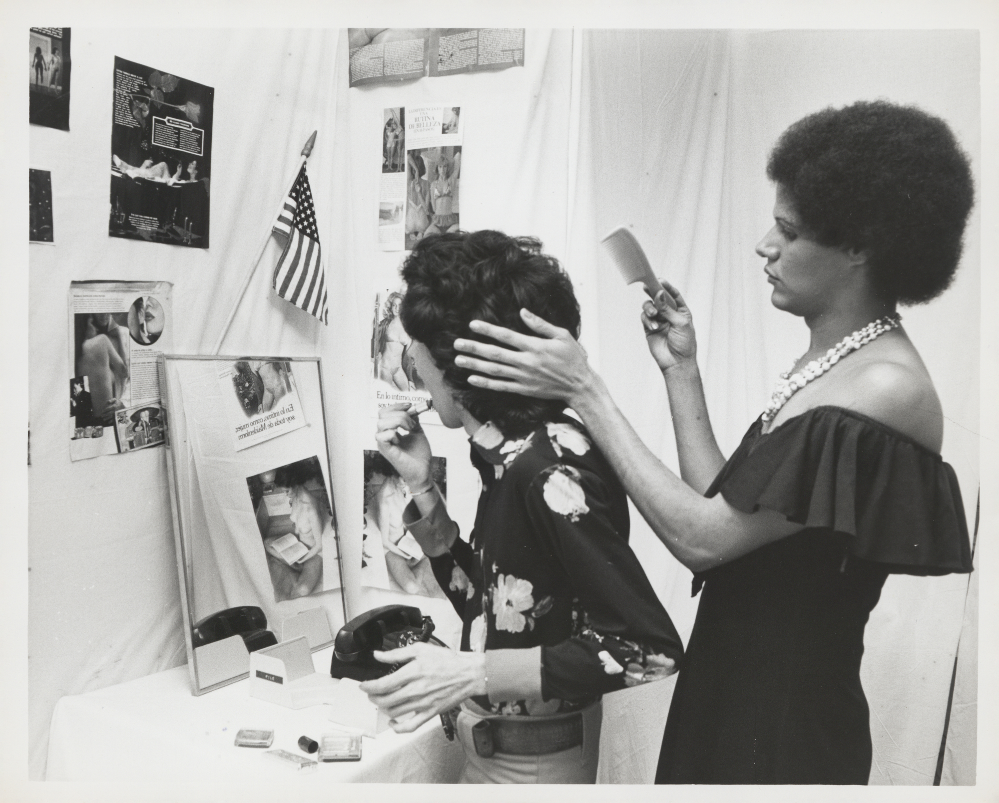 A black and white photograph of two gender non-conforming individuals applying makeup and grooming.