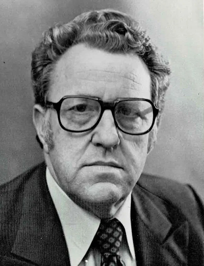 Black and white headshot of John Ward. He wear dark framed glasses and a suit