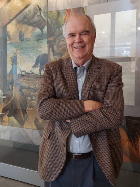 Color photograph of Bobby Roberts standing in front of the Joe Jones mural "Struggle in the South" at UA Little Rock Downtown
