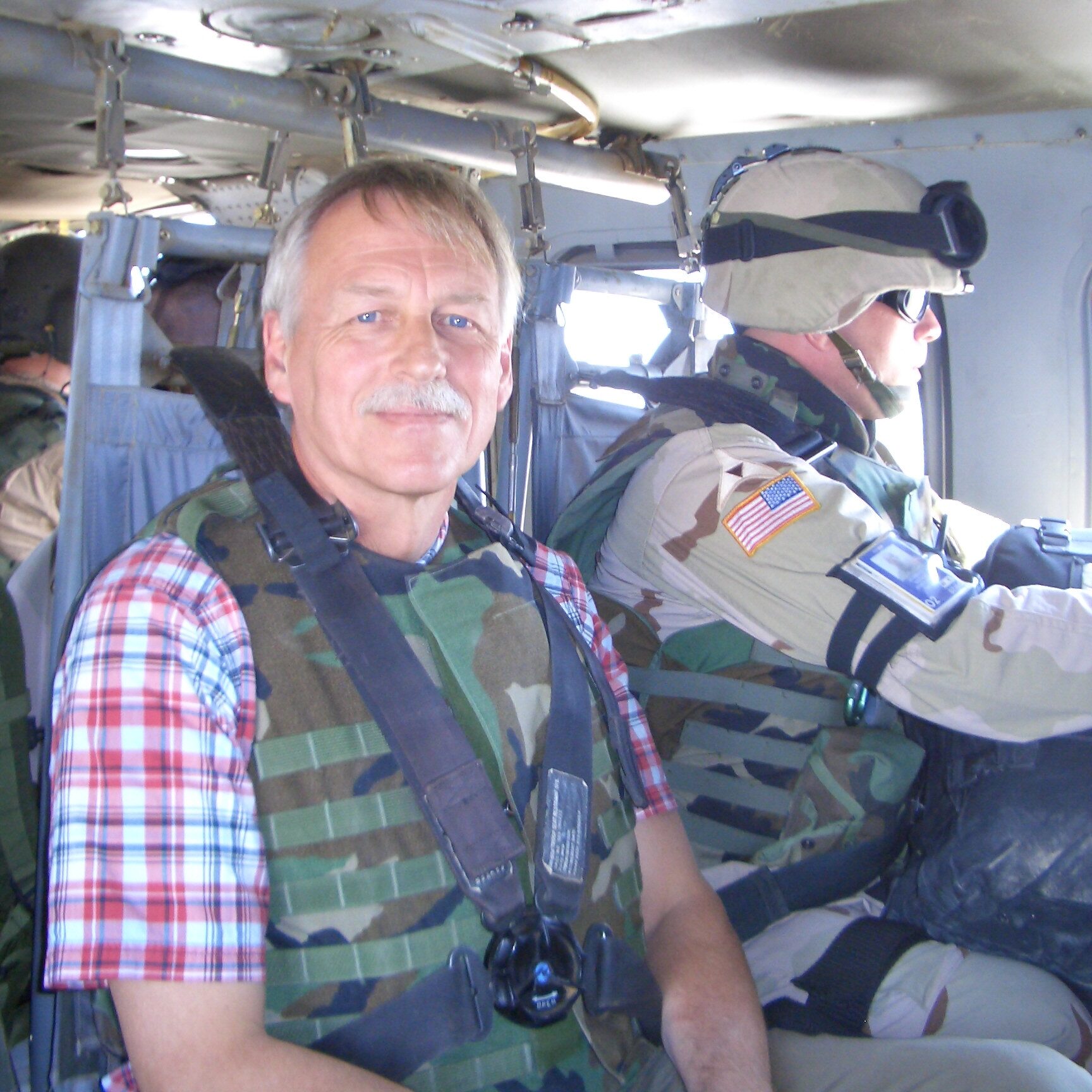 Snyder rides in a helicopter wearing a bulletproof vest. A gunman is seated beside him looking out the helicopter window