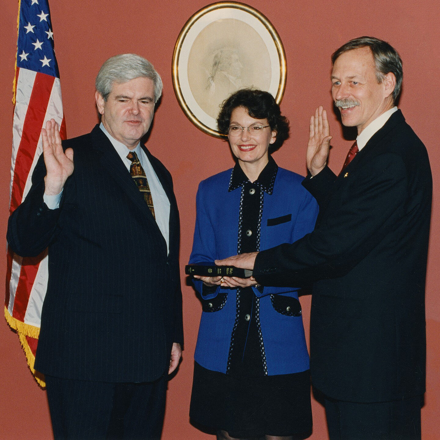 Color photograph of Debbie Milam holding a book. Vic Snyder and Newt Gingrich have one hand on the book and the other raised to their shoulder