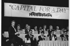 Jim Guy Tucker in front of cabinet and Capital for a Day sign in Harrison, Arkansas
