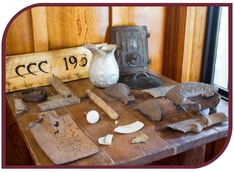 Color photograph of CCC artifacts on a table, including a sign and pottery shards
