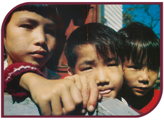 A color photograph of three Vietnamese boys standing next to each other behind a wooden stair railing