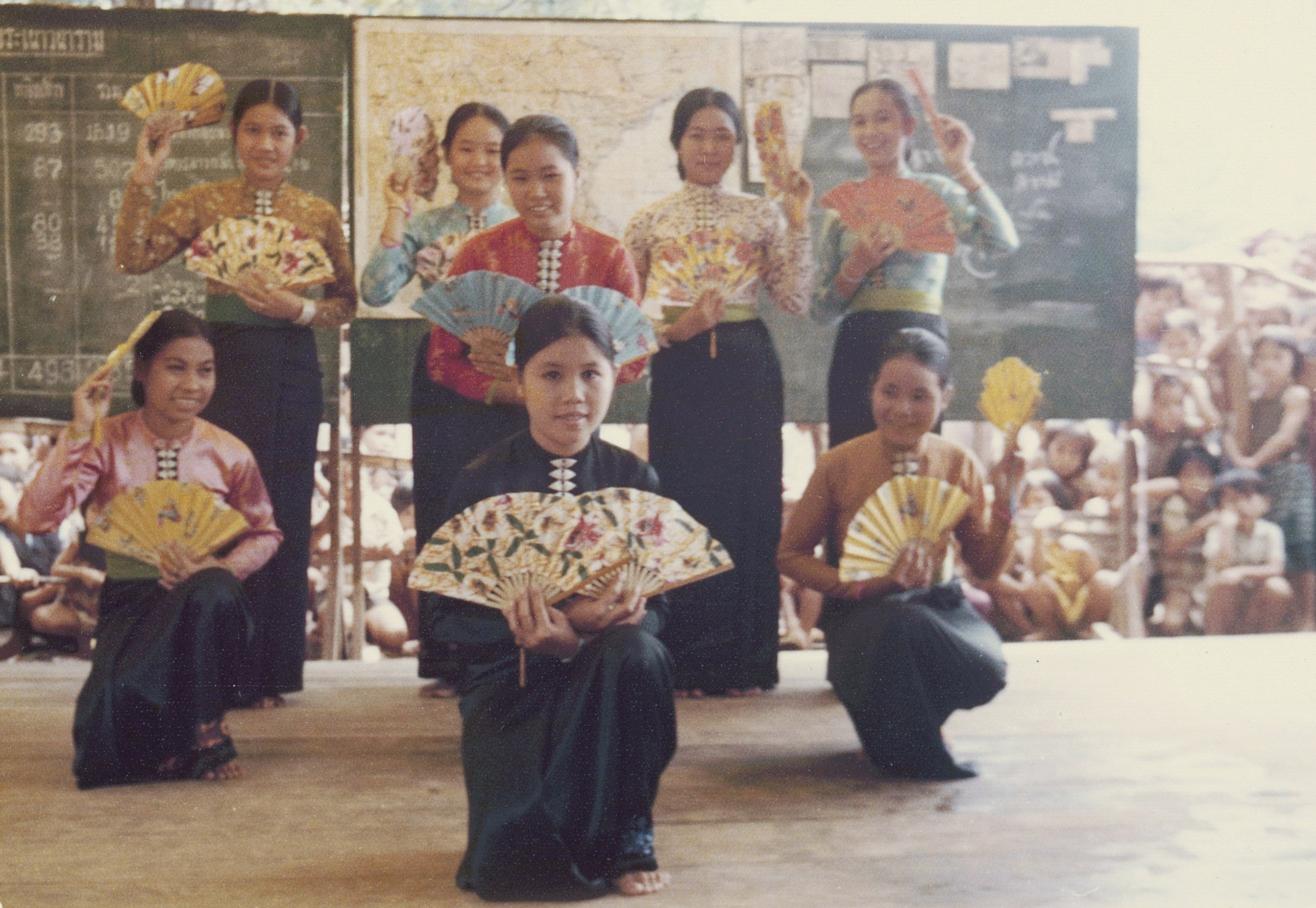 Color photograph of eight young Vietnamese women performing a fan dance in traditional costumes.