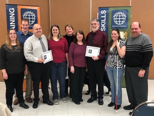 Two graduates from the Assistive Technology Instructor program pose with their wives and WSB staff, 31 January 2020