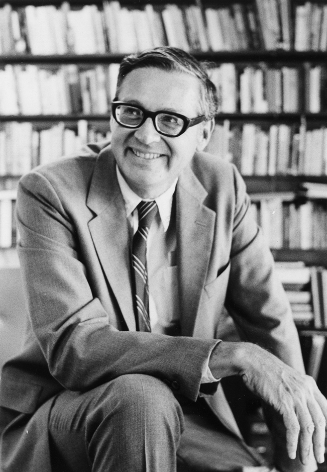 Black and white photograph of Cal Ledbetter, Jr. kneeling in front of shelves full of books.