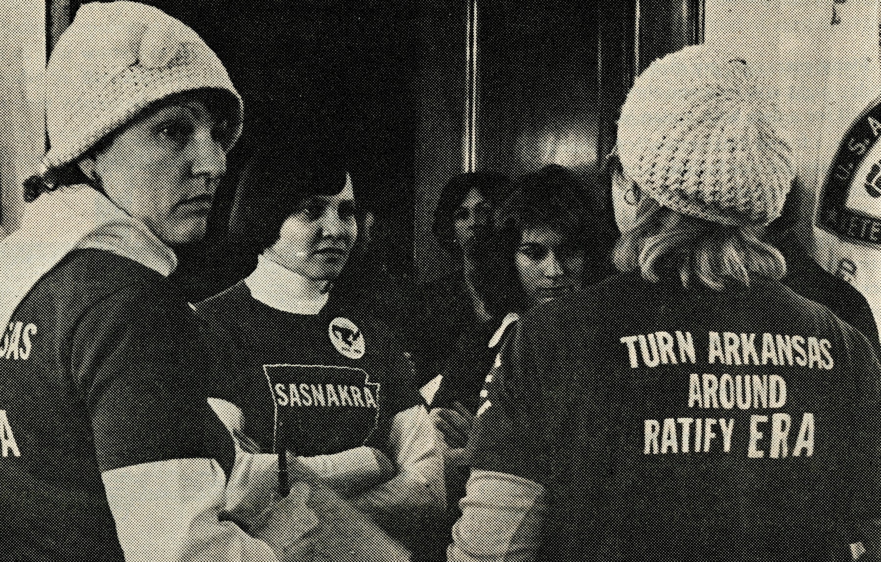 A group of women wear shirts that have a backwards Arkansas on the front and read "Turn Arkansas Around. Ratify ERA" on the back.