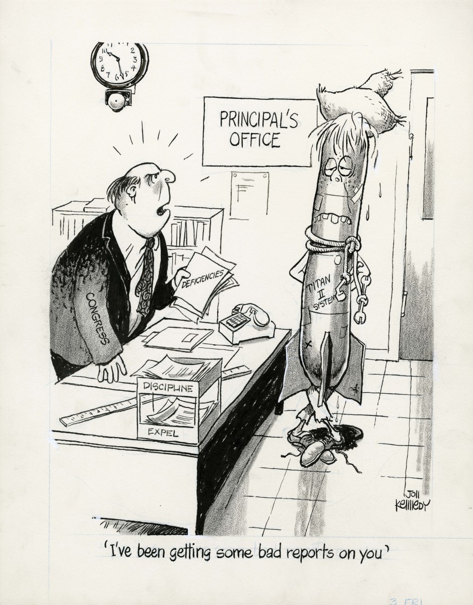 A battered and worn Titan II Missile wearing a straw hat and a wrench on a rope around its neck stands awkwardly in the principal's office.  The principal, representing Congress, holds a packet of papers with the word "deficiencies" on it. The principal says to the missile, "I've been getting some bad reports on you."
